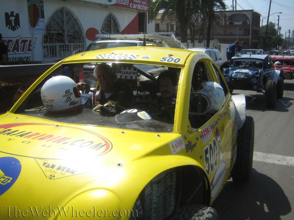 Yellow race car #500 with two people seated inside on a street