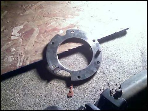1996 Ford F-150 - A metal flange part is shown on a textured surface, with a partial view of another metal component in the lower right corner.