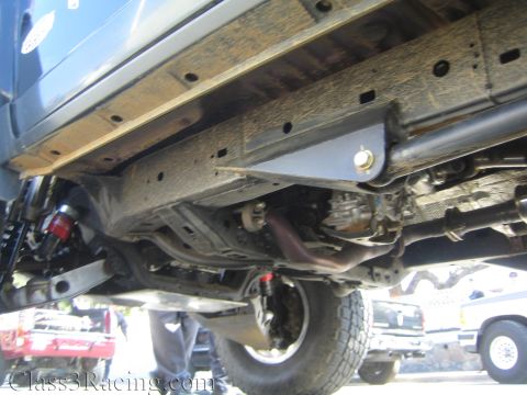 1990 Ford Bronco - Underbody view of an off-road vehicle exposing the frame rail, exhaust piping, shock and rear axle over a paved lot.