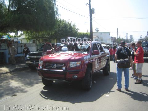 1990 Ford Bronco - red Honda Ridgeline race truck numbered 770 with roof light bar parked on a crowded street as people stand nearby.