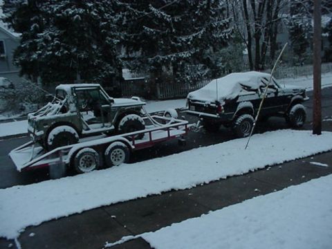 1992 Ford Bronco - A Suzuki Samurai is loaded onto a trailer, which is being towed by another vehicle in a snowy environment.