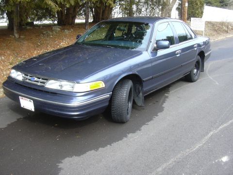 1996 Ford Crown Victoria - 1996 Ford Crown Victoria sedan parked on a wet road with trees in the background.