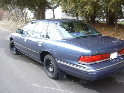 1996 Ford Crown Victoria - This blue sedan, identified as a 1996 Ford Crown Victoria, is parked on a residential street with trees in the background.