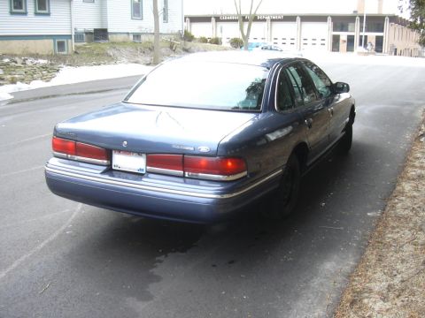 1996 Ford Crown Victoria - A blue sedan is parked on the side of the road with a fire department building in the background.