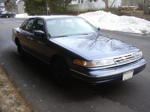 1996 Ford Crown Victoria - Dark blue sedan parked on asphalt, with snow visible in the background. Another car is in the distance.