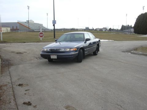 1996 Ford Crown Victoria - A dark blue 1996 Ford Crown Victoria is parked in front of a stadium on an overcast day.