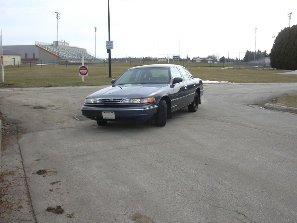 Dark blue 1996 Ford Crown Victoria parked on asphalt, stadium in background