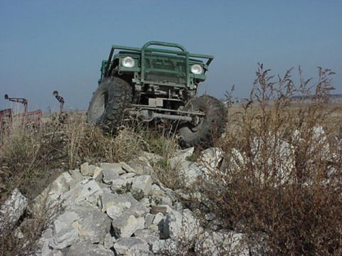 1992 Ford Bronco - This green off-road vehicle navigates a rocky terrain under a clear blue sky.