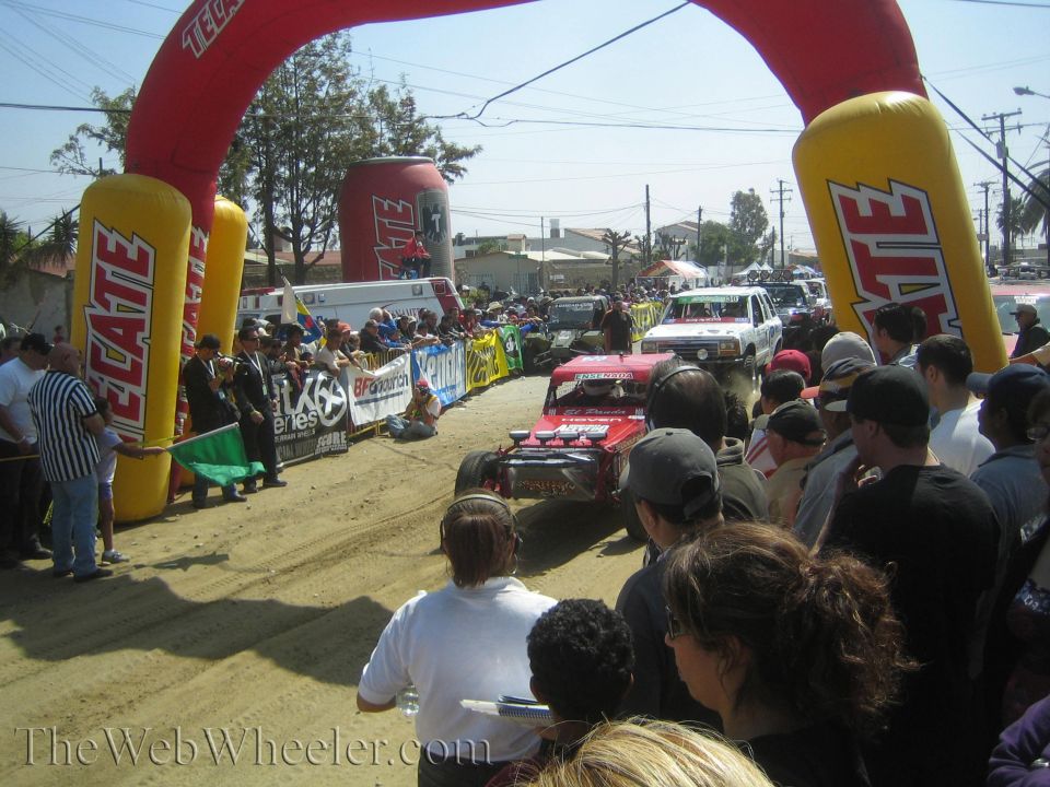 Race truck launching onto a dirt course under a Tecate start arch