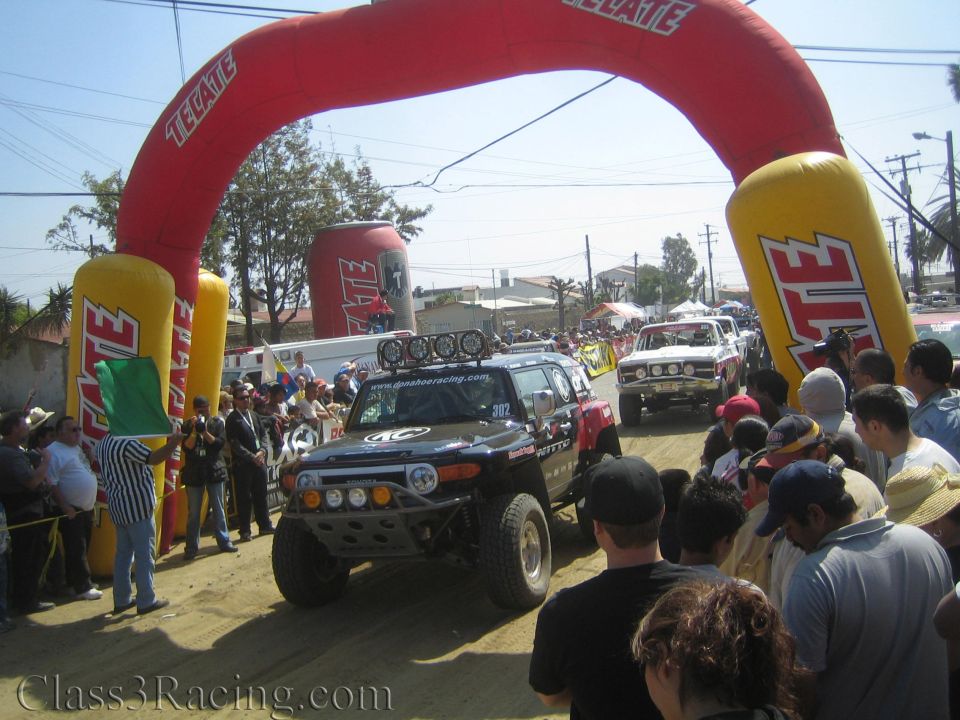 Black off-road race truck under red Tecate inflatable start arch