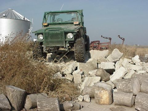 1992 Ford Bronco - A green off-road vehicle navigates a terrain of broken concrete and dry brush.