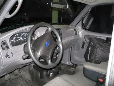 2003 Ford Ranger - The interior of a 2003 Ford Ranger shows the dashboard, steering wheel, and passenger seat with a bag.