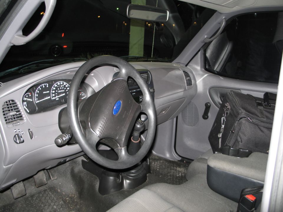 Gray 2003 Ford Ranger interior with a black steering wheel, dashboard, and gray seats. A black bag is on the passenger seat