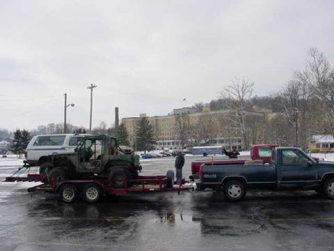1992 Ford Bronco - A pickup truck tows a trailer carrying an off-road vehicle in a snowy parking lot.