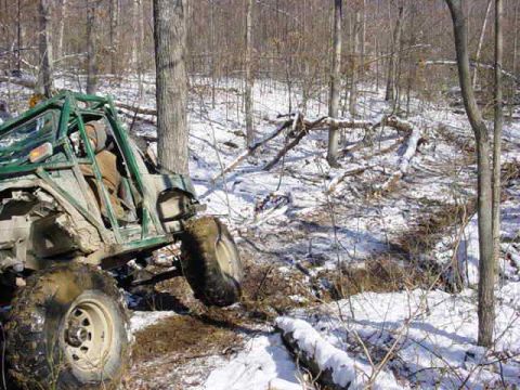 1992 Ford Bronco - An off-road vehicle navigates a snowy, wooded terrain, appearing stuck.