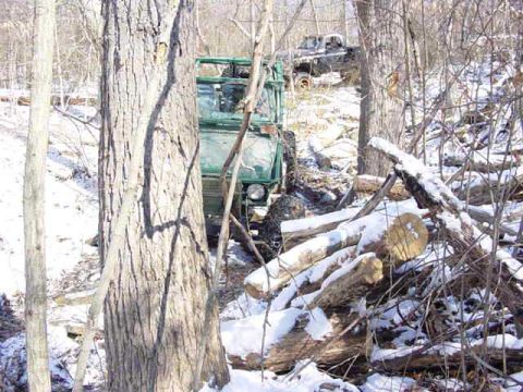 1992 Ford Bronco - Two off-road vehicles navigate a snowy, wooded terrain with fallen logs.