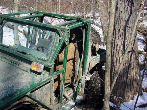 1992 Ford Bronco - This off-road vehicle is positioned precariously between two trees in a snowy, wooded environment.