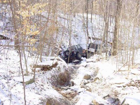 1992 Ford Bronco - Two off-road vehicles are stuck in a snowy, wooded ravine, indicating a difficult off-road situation.