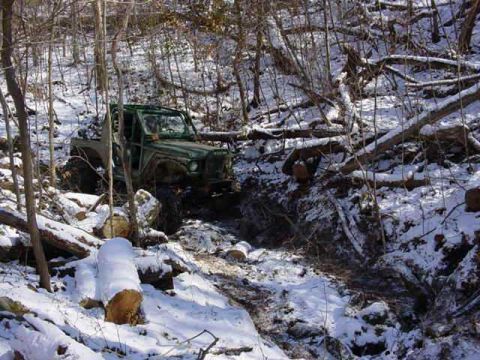 1992 Ford Bronco - Off-road vehicle traversing a challenging snowy path through dense woods.