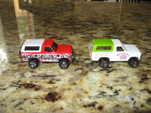 1986 Ford Bronco - Two toy trucks are displayed on a speckled countertop.