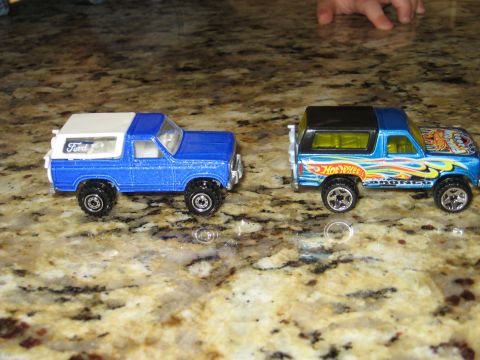 1986 Ford Bronco - Two toy Ford Bronco models are displayed side-by-side on a speckled countertop.