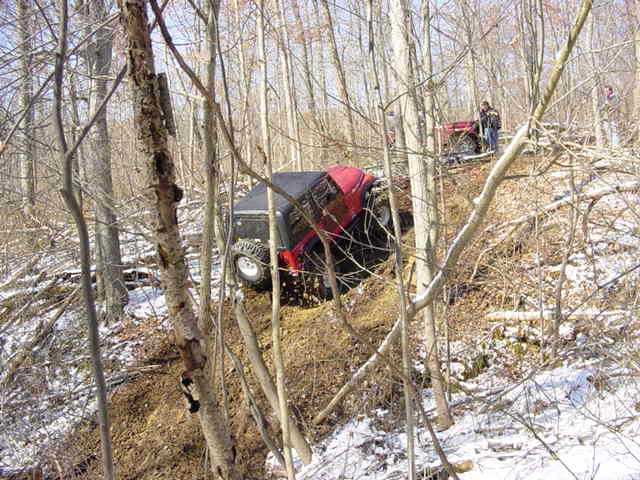 Red and black off-road vehicle tilted on a snowy hill with another vehicle behind it