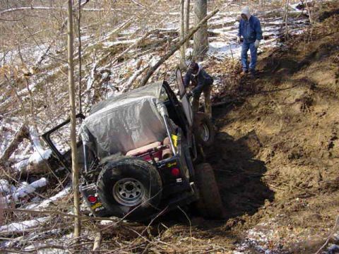1992 Ford Bronco - A Jeep Wrangler is stuck on a steep, muddy incline with two people observing.