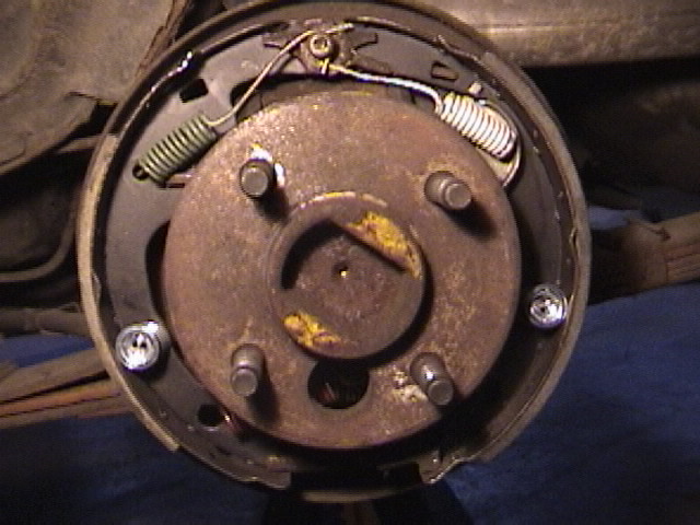 Disassembled drum brake backing plate with shoes and springs on a vehicle