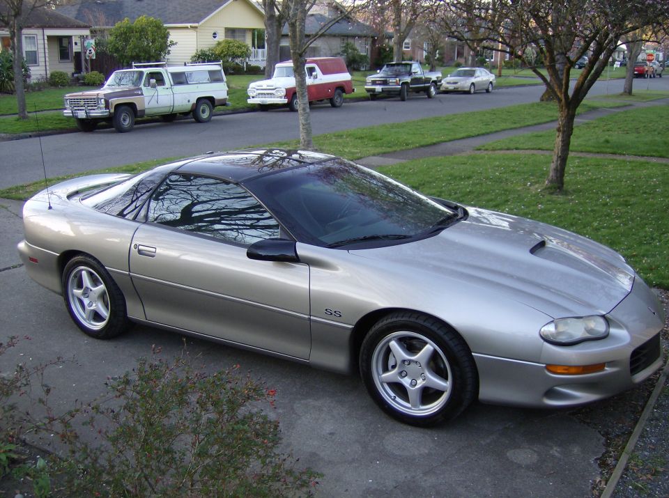 Silver Chevrolet Camaro SS parked in driveway, other vehicles and houses in background