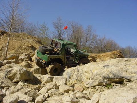 1992 Ford Bronco - A green off-road vehicle tackles a challenging rocky incline under a clear blue sky.