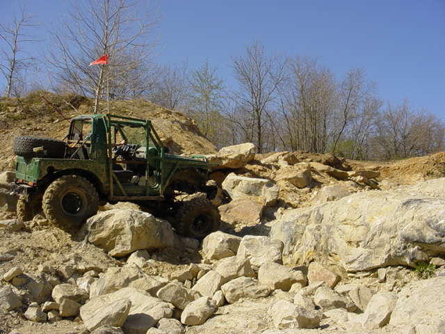 Green off-road vehicle with a spare tire on the back, navigating a rocky trail