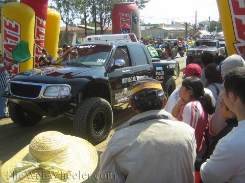 1990 Ford Bronco - black off-road race truck numbered 1504 with Motoraz Racing decals waits in a staging lineup as spectators crowd the rail.