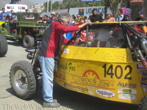 1990 Ford Bronco - yellow tube-frame off-road buggy numbered 1402 covered in fan signatures and El Dorado Ranch decals as a man leans over it.