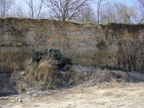 1992 Ford Bronco - A modified off-road vehicle is positioned on a rough terrain near a large rock formation.