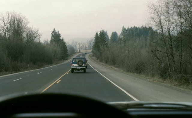 Dark SUV with rear spare tire driving ahead on a rural two-lane highway, seen through windshield