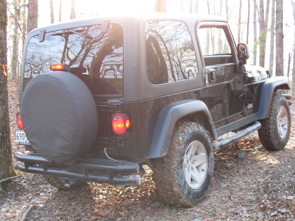Black Jeep Wrangler hardtop parked in wooded area, rear three-quarter view