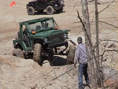 1992 Ford Bronco - Two off-road vehicles navigate a rocky, dirt course with a man observing.