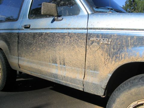 1990 Ford Bronco II - A light blue SUV, heavily soiled with mud, is viewed from the side, revealing its door and fender details.
