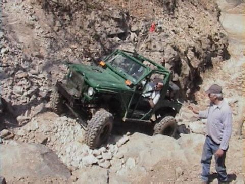 1992 Ford Bronco - A green off-road vehicle maneuvers through a challenging rocky landscape with a person observing.