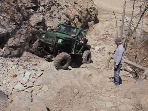 1992 Ford Bronco - A green off-road vehicle tackles a challenging rocky incline with a person observing.