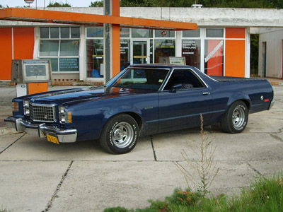 1973 Ford Ranchero - A blue 1973 Ford Ranchero pickup truck is parked in front of a building with orange trim.