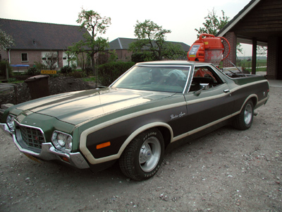 1973 Ford Ranchero - A 1973 Ford Ranchero is parked in a gravel driveway with a building in the background. A pump is strapped to the roof.