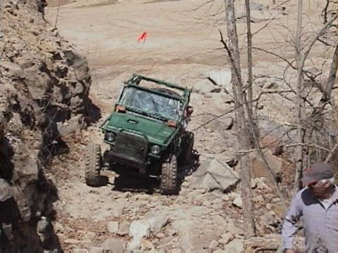 1992 Ford Bronco - Off-road vehicle climbing a steep, rocky incline with trees and sparse vegetation.