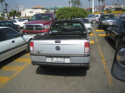 1990 Ford Bronco - Rear view of a silver Volkswagen Pointer compact pickup in a parking lot, with a red Dodge Ram and other cars nearby.
