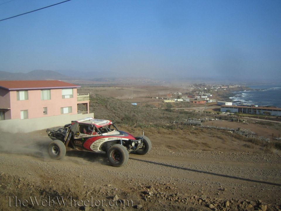 Off-road race buggy kicking up dust on a dirt road above a coastal town