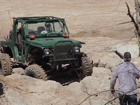 1992 Ford Bronco - A modified green off-road vehicle is shown traversing a challenging, rocky landscape.