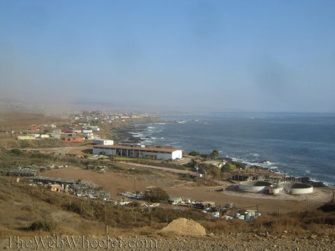 1990 Ford Bronco - small coastal town with low buildings spreads along a rocky shoreline below a hilltop, with haze hanging over the ocean.