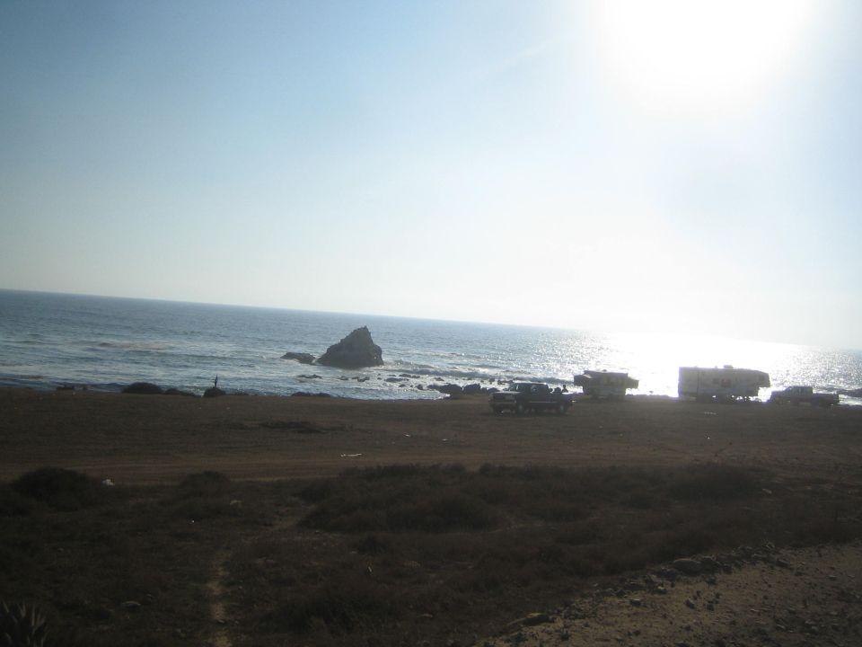 Beach campsite with RVs and vehicles by the ocean under a bright sun
