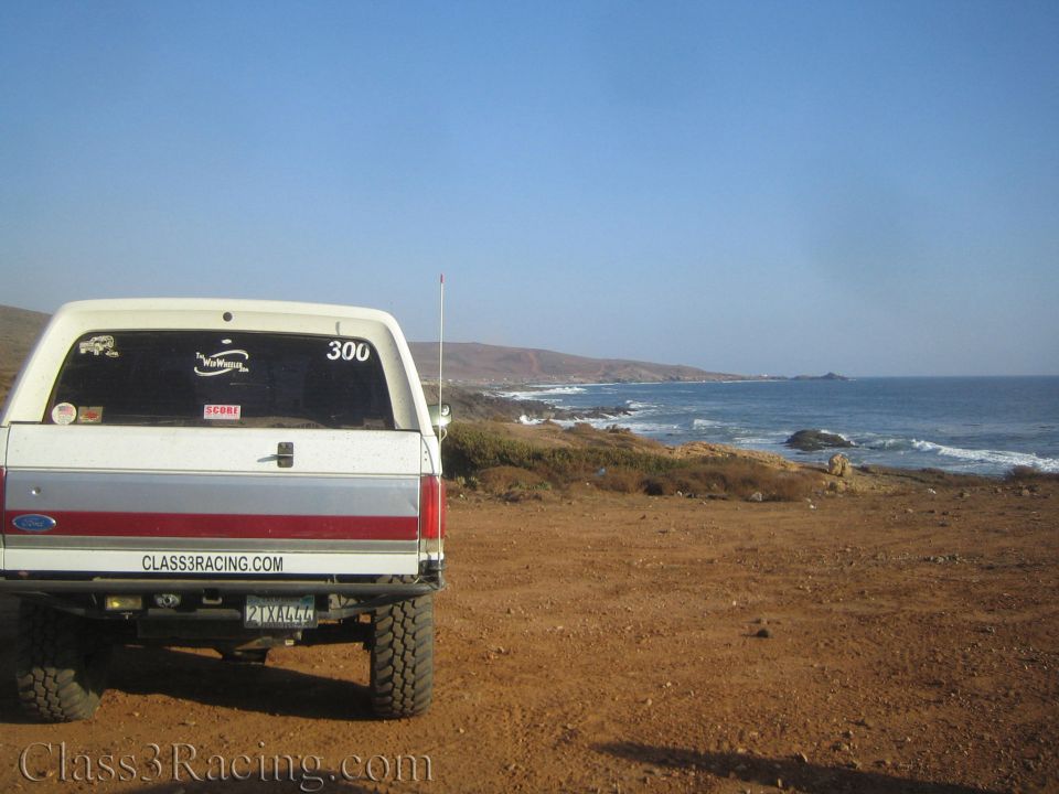 Rear of a white lifted pickup truck parked at a desert coastline overlook