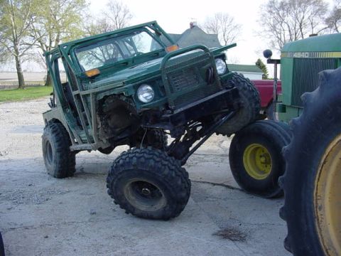 1992 Ford Bronco - An off-road vehicle is parked next to a tractor on a dirt lot.